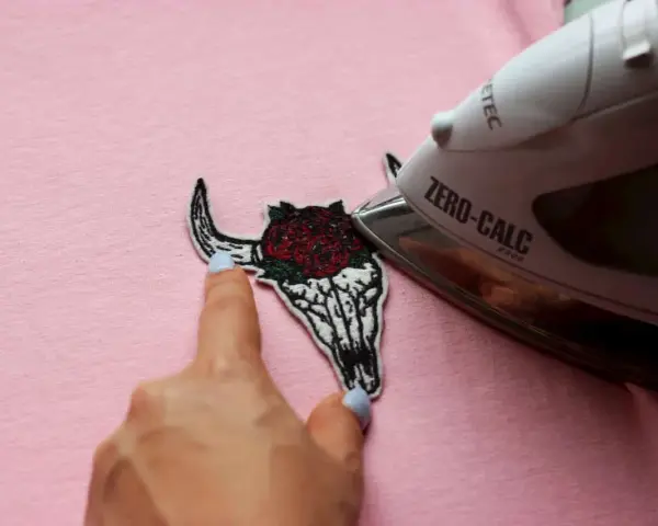 Come attaccare toppe termoadesive: un teschio di toro con rose viene stirato su una maglietta rosa.