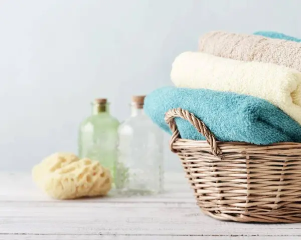 Cesto di vimini con asciugamani morbidi, come i rimedi della nonna. Accanto, spugna naturale e bottiglie di vetro.