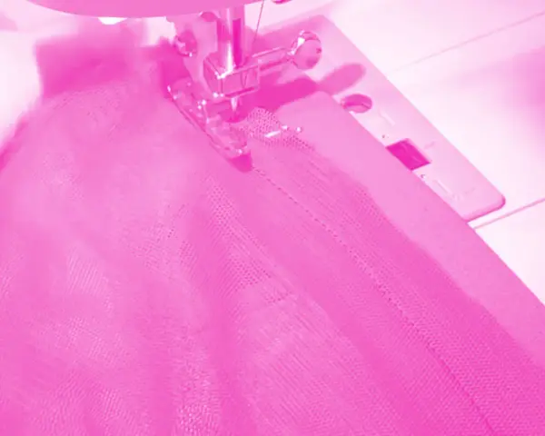 Macchina da cucire al lavoro per cucire una gonna di tulle rosa.