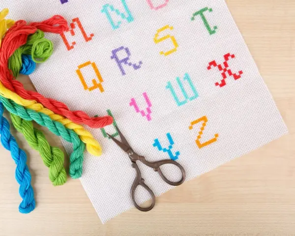 Fili colorati e forbicine pronti per ricamare nomi punto catenella su tela bianca con lettere dell'alfabeto.