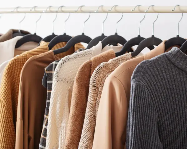 Una fila di capi d'abbigliamento in tonalità neutre, tra cui un maglione lavorato a maglia e un blazer in tessuto cupro lavaggio, pronti per essere indossati.