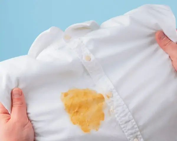 Come togliere le macchie gialle dalla biancheria colorata: una camicia bianca macchiata di giallo, tenuta in mano.