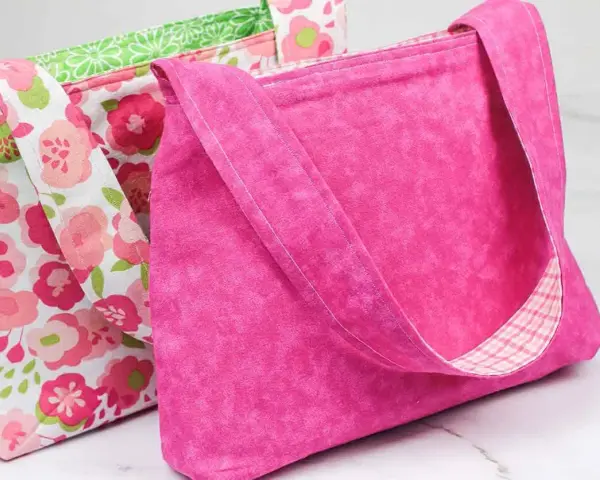 Two handmade fabric bags, one pink with a floral pattern, the other solid pink with a plaid lining.