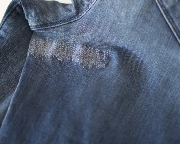 Dettaglio di un tessuto di jeans blu con un'area rattoppata con filo bianco, che mostra la cura nel rattoppare jeans.