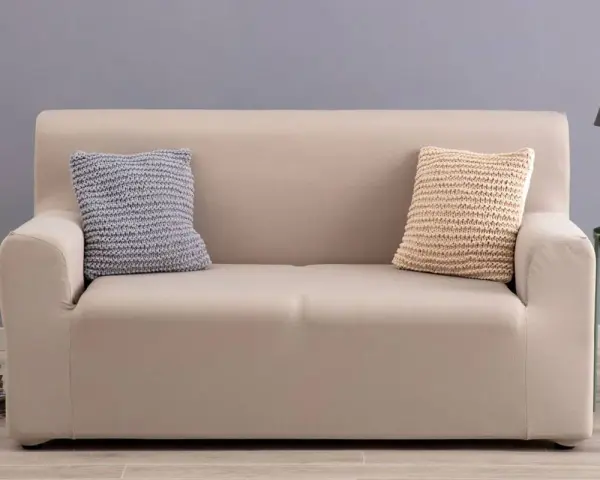 Divano con copridivano in tessuto color crema, due cuscini decorativi a maglia, uno grigio e uno beige.