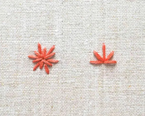Two orange embroidery stitches on a textured linen fabric.