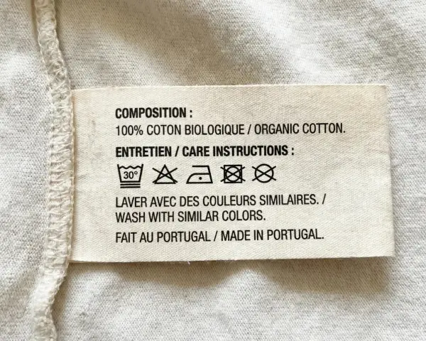 Etichetta con simboli tessuti: lavaggio 30°, non candeggiare, stirare a bassa temperatura, non lavare a secco, non asciugare in asciugatrice. 100% cotone biologico, fatto in Portogallo.