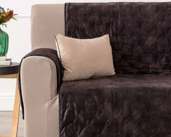 Divano con copridivano trapuntato marrone scuro, un cuscino beige e un vaso di fiori. Il miglior tessuto per divani per un look accogliente.