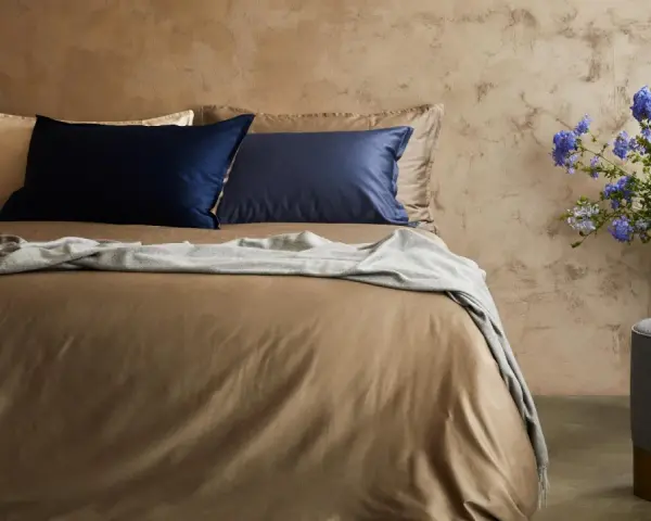 Letto con lenzuola color tabacco, cuscini blu e beige, coperta grigia. Il miglior tessuto per lenzuola per un sonno di qualità.