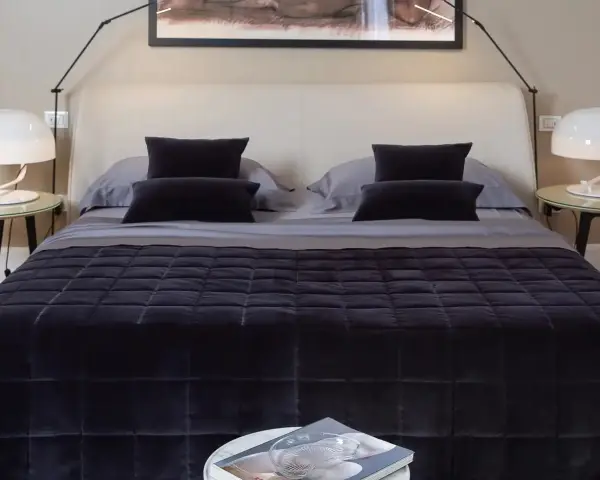 Un letto impeccabile, con copriletto trapuntato scuro e cuscini coordinati, mostra come rifare il letto in modo elegante.