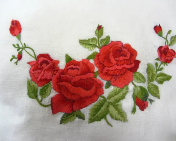Ricamo di rose rosse su tessuto bianco, un delicato punto pittura che evoca un giardino fiorito.