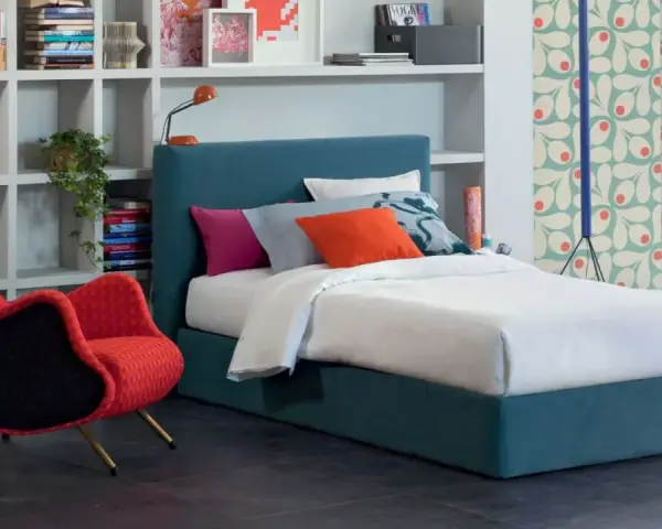 Letto una piazza e mezza con testiera blu, cuscini colorati e una poltrona rossa vivace.
