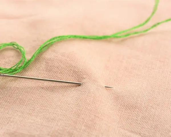 Ago e filo verde pronti per ricamare nome a mano su stoffa color pesca.