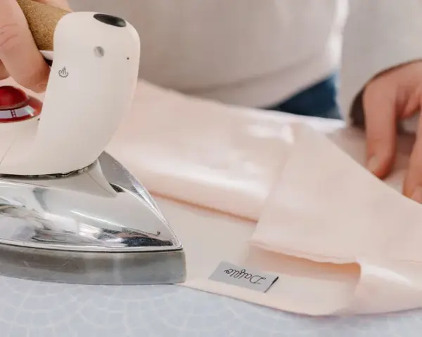 Mani che stirano lenzuola rosa pallido con un ferro da stiro Immetec. Un'etichetta con il logo "Daffodil" è visibile sul tessuto.