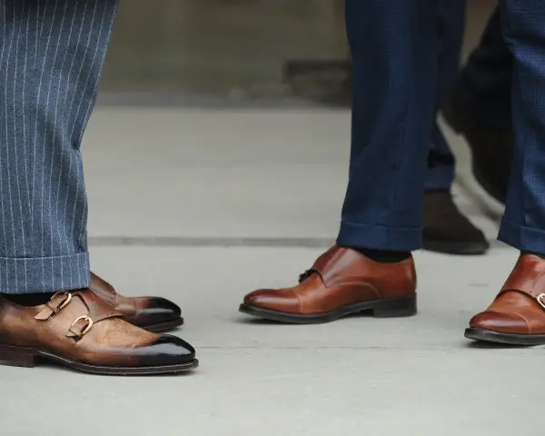 Primo piano su scarpe monk strap marroni e diversi tipi di orlo pantaloni: a risvolto e con pinces.