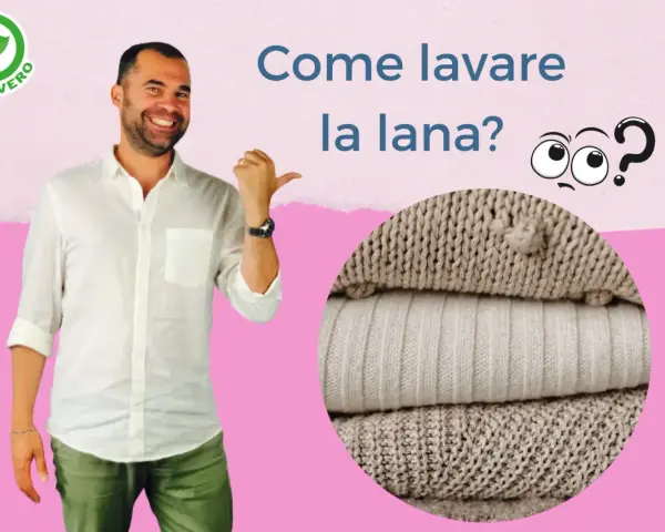 Uomo sorridente indica come lavare lana a mano. Pile di maglioni in primo piano.