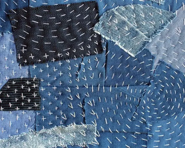 Tessuto patchwork in denim con cuciture bianche a punto croce e a zig-zag, un esempio di rammendo giapponese.