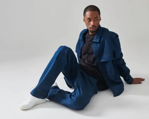 Un uomo con un completo di jeans blu, seduto a terra. Chissà quanto pesa un paio di jeans così comodi.