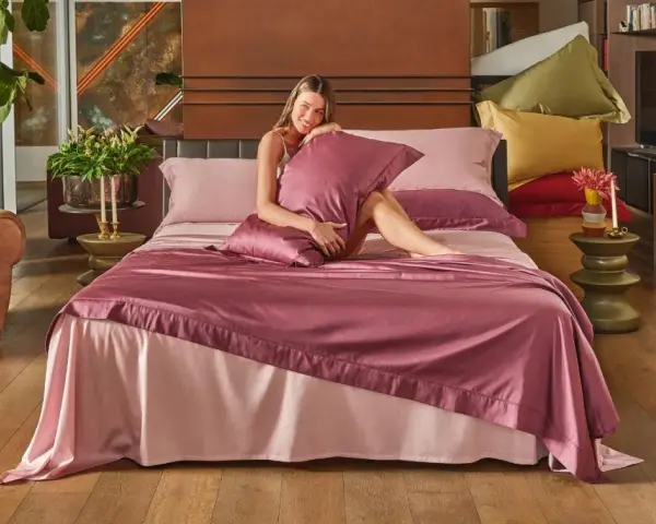 Donna sorridente su un letto con lenzuola rosa. Scopri come lavare le lenzuola nuove per mantenerle morbide e fresche.
