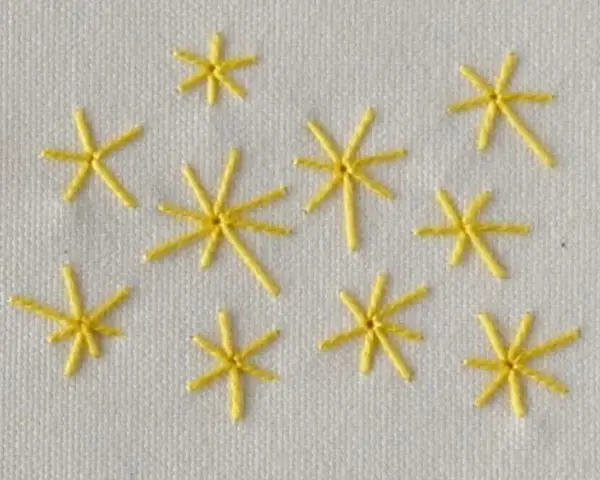 Piccole stelle gialle ricamate a punto pieno su tessuto bianco. Un esempio di come ricamare una stella a punto pieno.