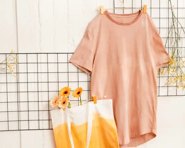 T-shirt rosa e borsa con sfumature arancioni, ispirazione per come tingere un vestito. Fiori e rametti secchi decorano.