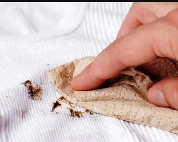 Dita che tamponano macchie marroni su biancheria antica con un tovagliolo di carta.