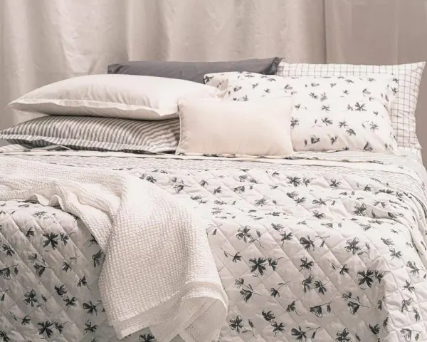 Un letto accogliente con biancheria a fiori e righe, coperte morbide e cuscini che invitano al riposo, come in un sogno di letti all'americana.