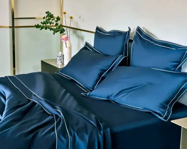 Letto matrimoniale con copriletto blu scuro e cuscini coordinati, rifiniti con bordi bianchi. Ideale per conoscere le misure copriletto matrimoniale.