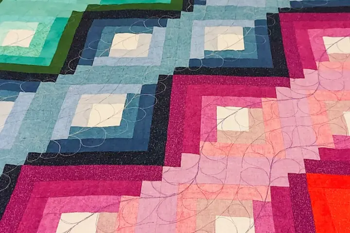 Dettaglio di una coperta realizzata con la tecnica patchwork, con blocchi a gradiente di colore dal blu al rosa, rifinita con cuciture decorative.