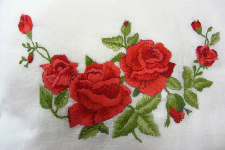 Ricamo di rose rosse su tessuto bianco, un delicato punto pittura che evoca un giardino fiorito.