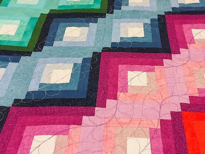 Dettaglio di una coperta realizzata con la tecnica patchwork, con blocchi a gradiente di colore dal blu al rosa, rifinita con cuciture decorative.