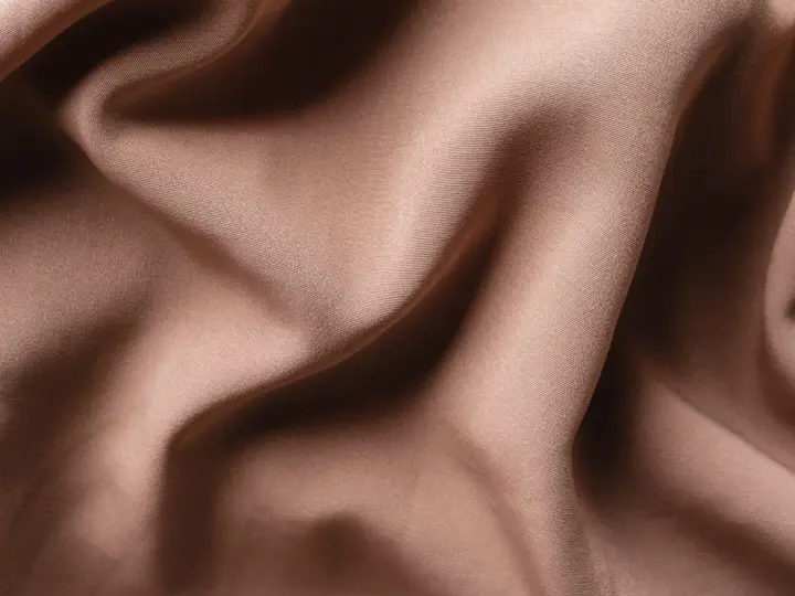 Tessuto di raso color tortora, morbido e drappeggiato, che mostra la sua texture fine. Il raso si può stirare per ottenere una finitura impeccabile.