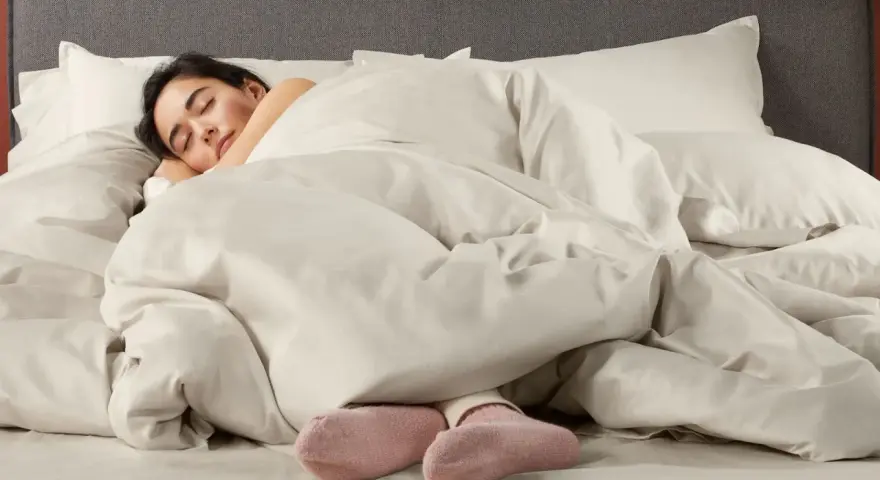 Donna dorme avvolta in lenzuola in microfibra che sembrano farla sudare, con solo i piedi in calzini rosa visibili.