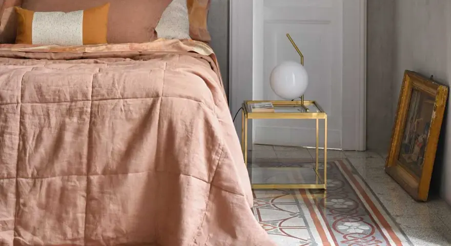 Un morbido quilt matrimoniale color pesca, con cuciture a quadri, adorna un letto in una stanza elegante.