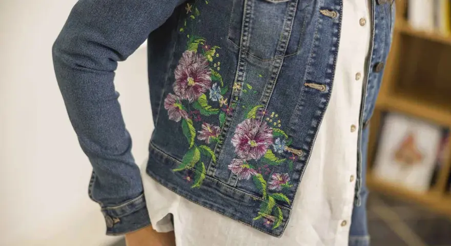 Giacca di jeans con un bellissimo ricamo su stoffa di fiori colorati e foglie verdi.