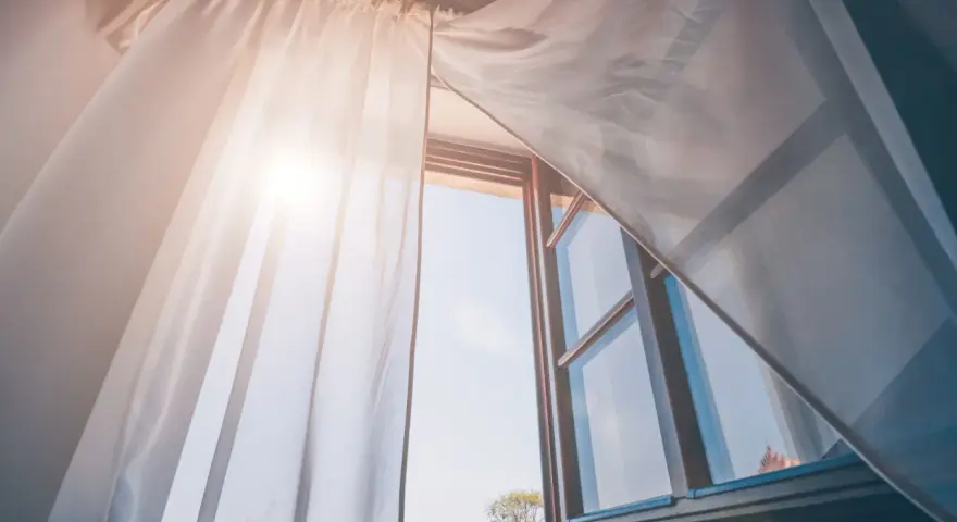 Tende leggere e ariose, fissate senza fare buchi, fluttuano dolcemente con la brezza che entra da una finestra aperta, illuminata dal sole.
