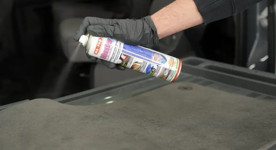 Mano con guanto nero spruzza spray Idrostop su tessuto grigio per impermeabilizzare.