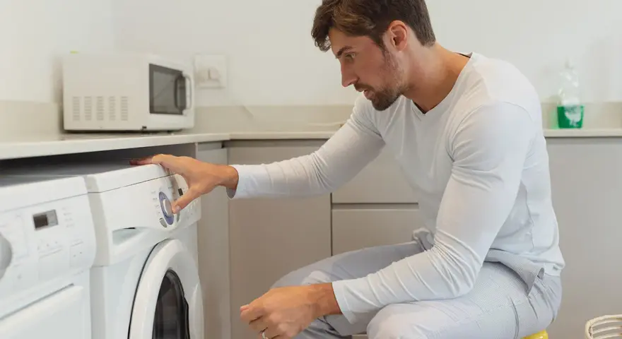 Uomo in pigiama imposta la lavatrice per asciugare la ciniglia.