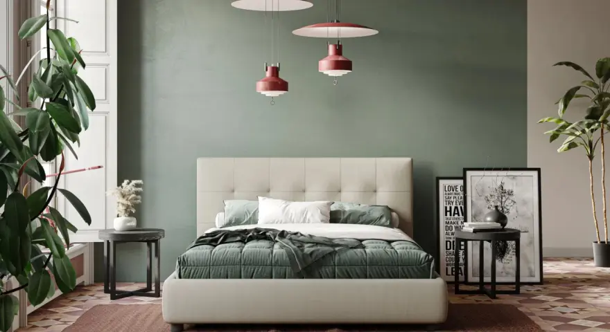 Letto moderno con testiera capitonné, copriletto verde e cuscini bianchi. Parti del letto ben visibili, con comodini e piante.