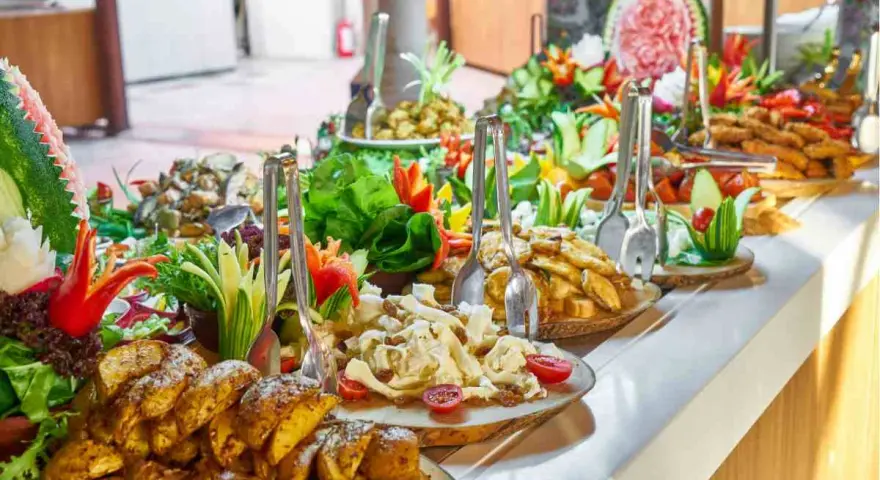 Buffet con patate arrosto, insalate fresche e frutta intagliata. Ecco come mettere la tovaglia per buffet, creando un'atmosfera invitante.
