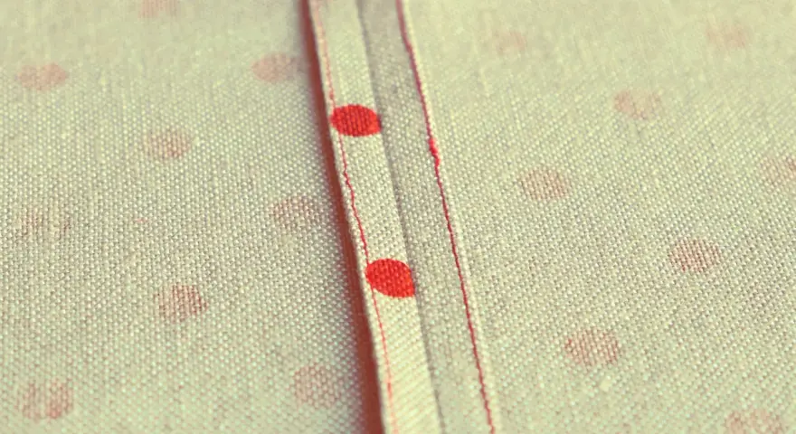 Tessuto a pois rossi con cucitura a vista, un punto per rifinire bordi con precisione sartoriale.