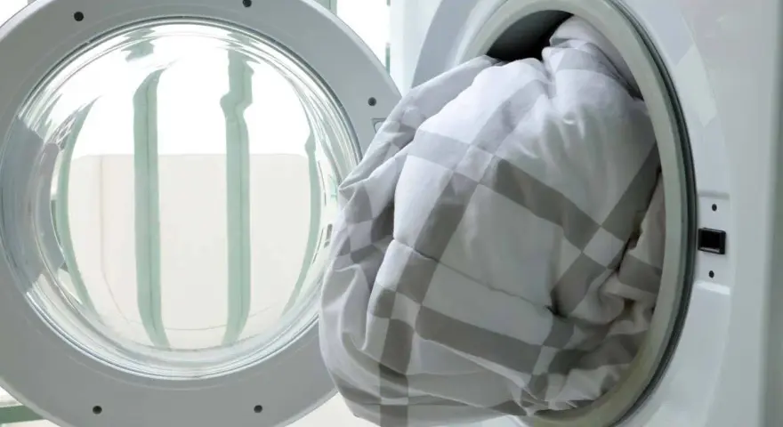 A white and grey checkered duvet being loaded into a washing machine.