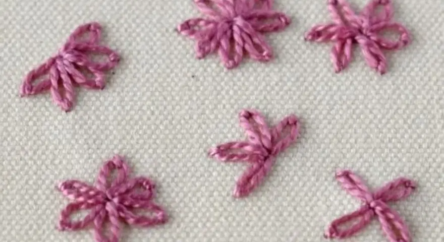 Close-up of five small, pink embroidered daisy stitches on a cream fabric background.