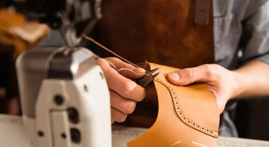 Mani esperte che cuciono la pelle con filo e ago, creando un dettaglio decorativo su un pezzo di cuoio.