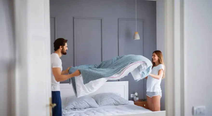 Coppia felice che cambia le lenzuola, un gesto che ci ricorda ogni quanto cambiare le lenzuola per un sonno più sano.