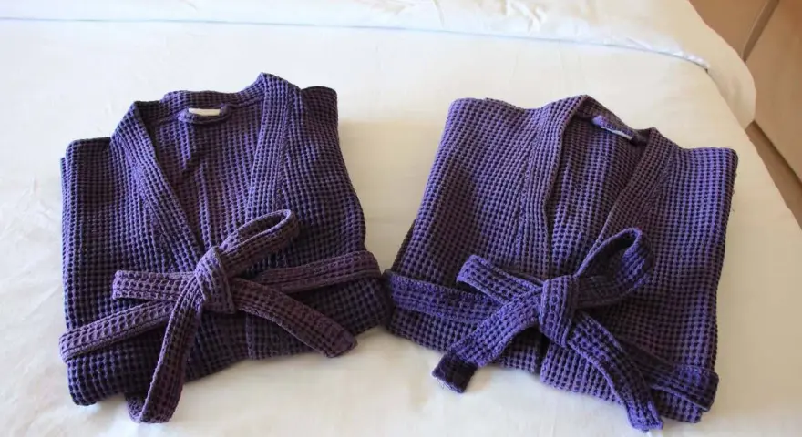 Due accappatoi viola, piegati e legati con la loro cintura, pronti per essere riposti. Ecco come piegare un accappatoio per un riordino perfetto.