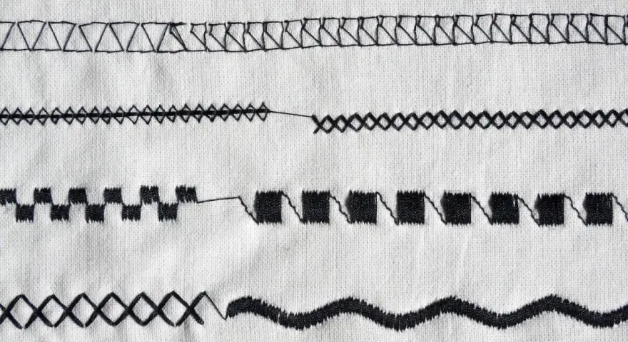 Close-up of various black sewing machine stitches on white fabric.