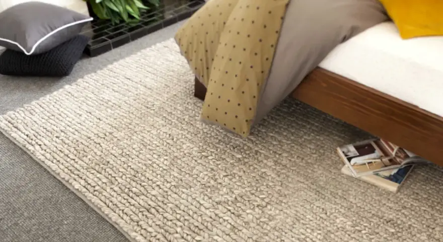 Un grande tappeto di lana intrecciata accanto a un letto. Scopri come lavare un tappeto di lana grande per mantenerlo come nuovo.
