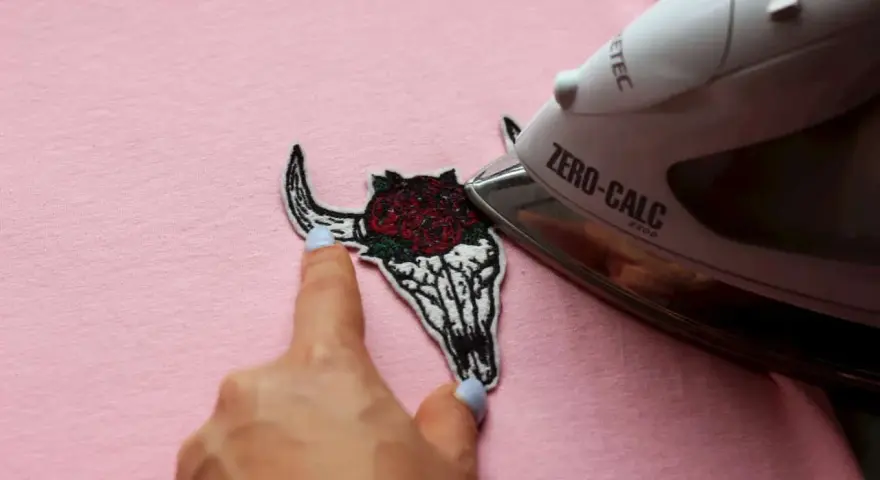 Come attaccare toppe termoadesive: un teschio di toro con rose viene stirato su una maglietta rosa.