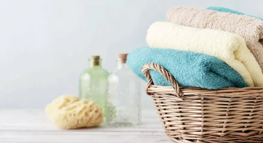 Cesto di vimini con asciugamani morbidi, come i rimedi della nonna. Accanto, spugna naturale e bottiglie di vetro.